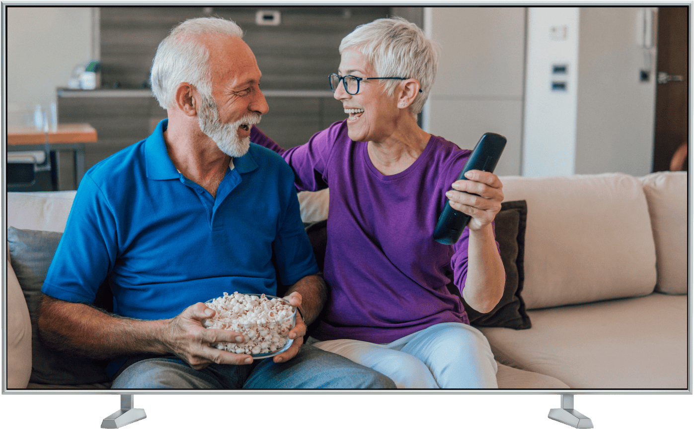 älteres, fröhliches Paar auf Couch mit Popcorn und Fernbedienung. Bild in TV-Rahmen